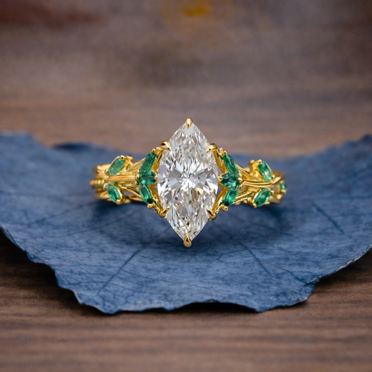 Gold ring with a large diamond and smaller emeralds on a blue leaf