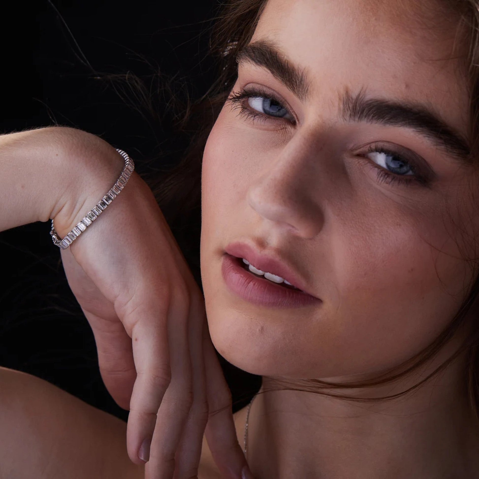 Close-up of a woman wearing a diamond bracelet with a dark 