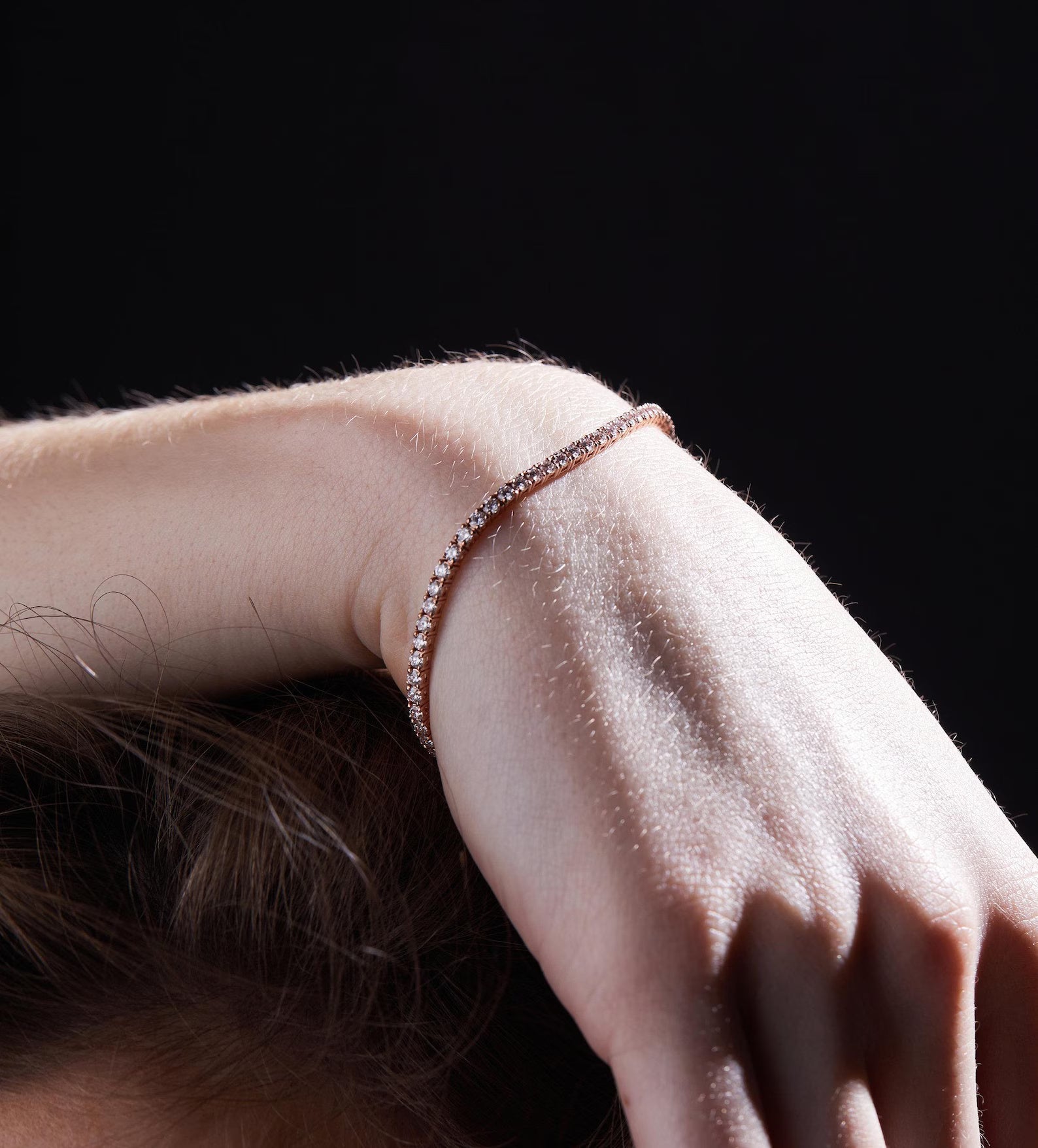 Close-up of a person's arm wearing a delicate bracelet against a dark 