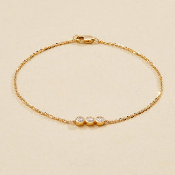 Gold bracelet with three small round diamonds on a beige 
