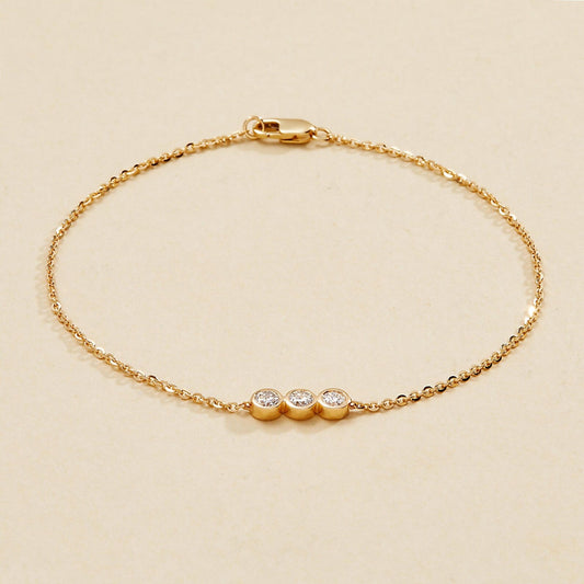 Gold bracelet with three small round diamonds on a beige 