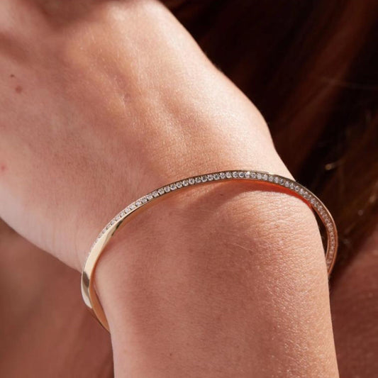 Close-up of a person's arm wearing a rose gold bracelet with small stones.