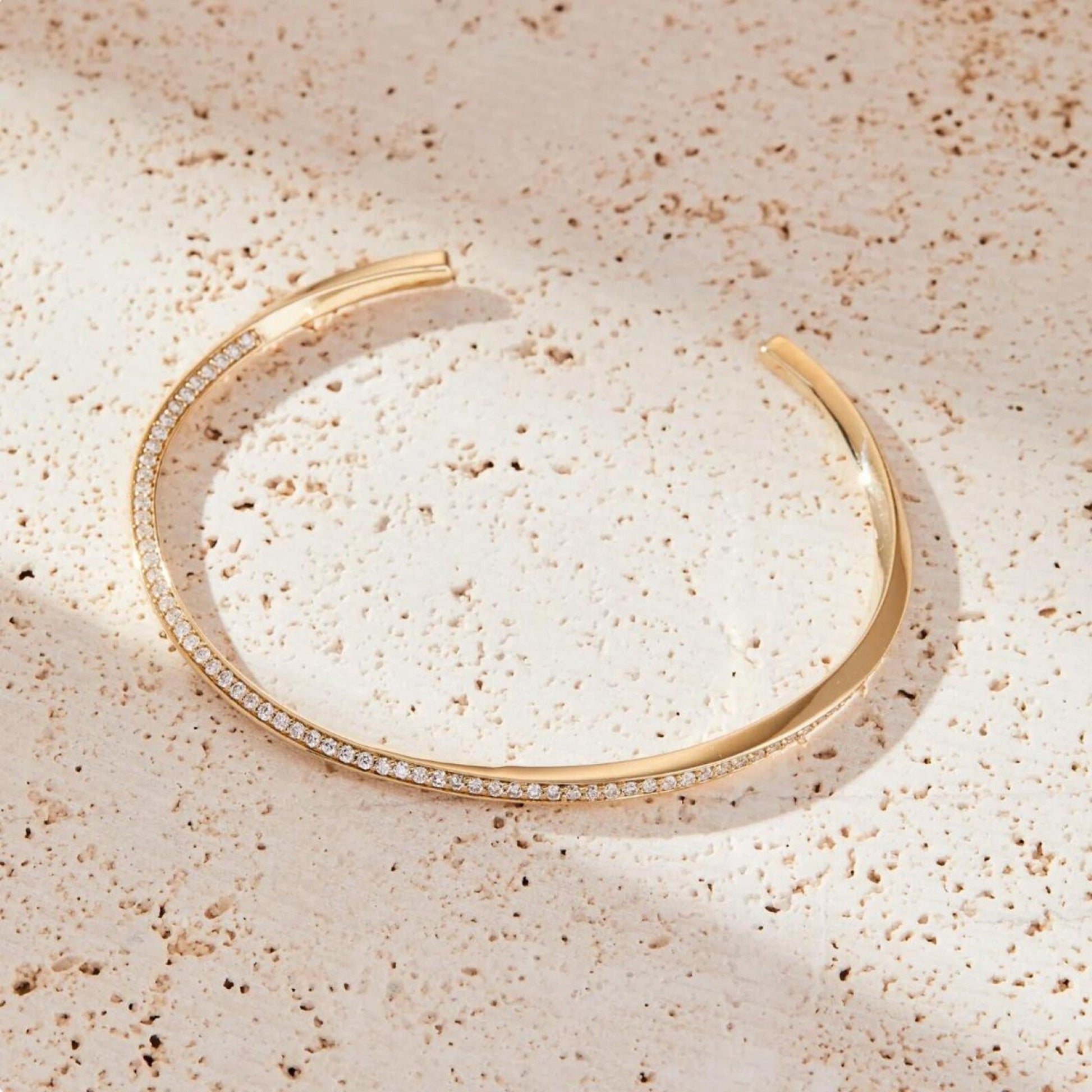 Gold bracelet with small diamonds on a beige textured surface